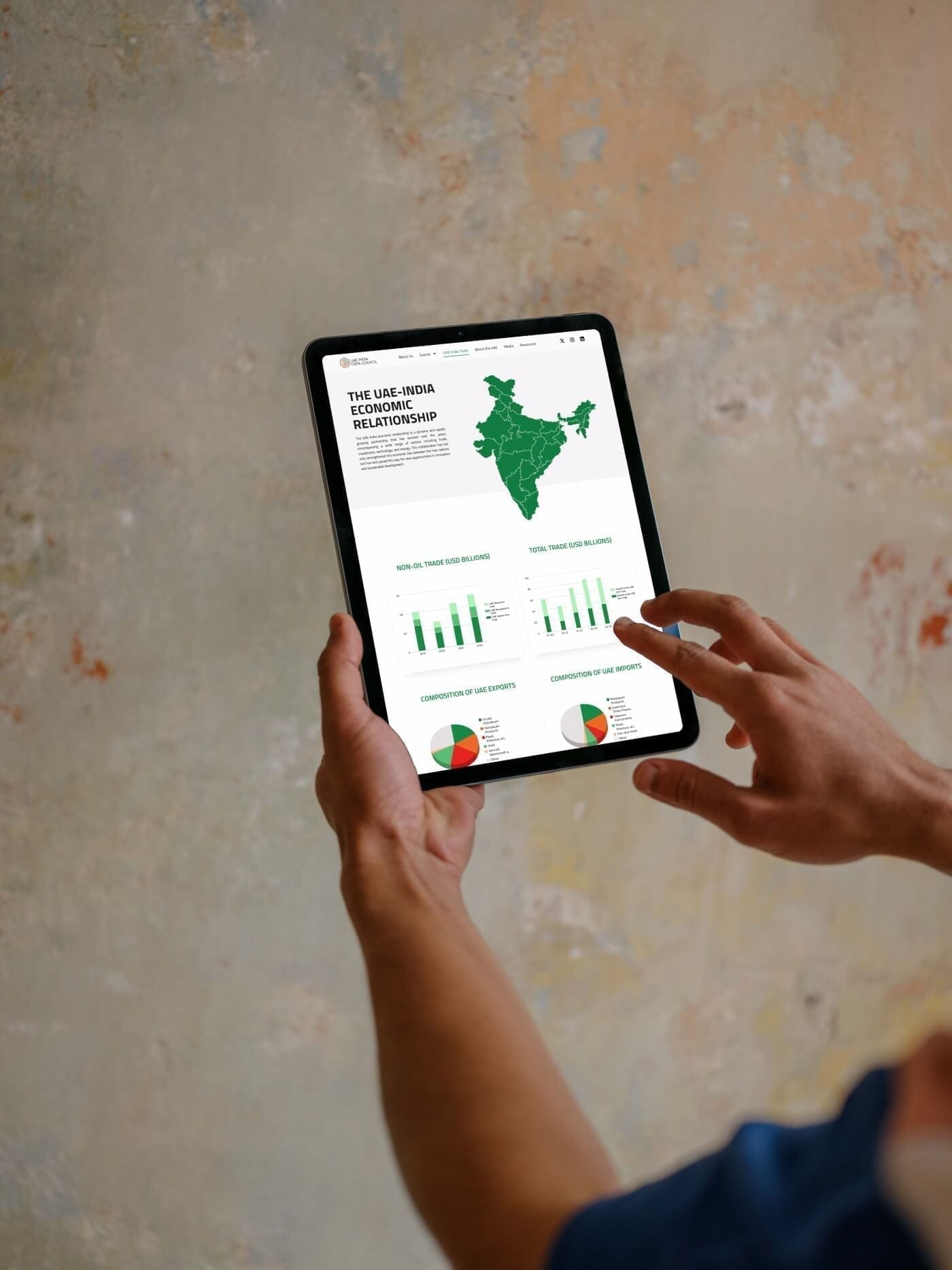 Hands holding a tablet showing the UAE–India Economic Relationship page, with a map of India and bar charts.