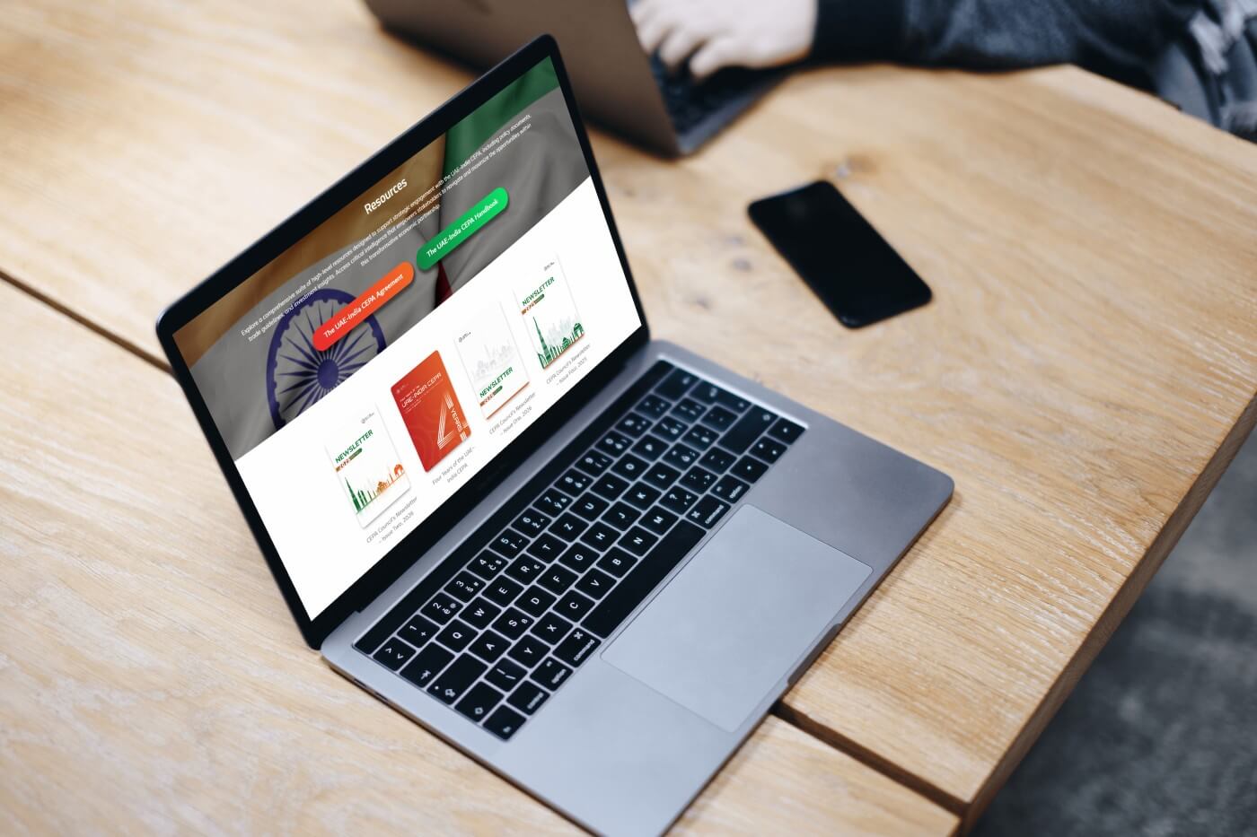 A laptop on a wooden table showing the Resources page, with a phone lying beside it.